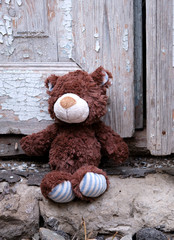 little teddy bear sits on the doorstep near an old door with cracked paint,