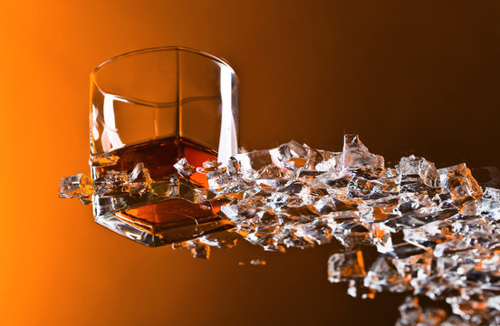 Glass of Whiskey with ice on a glass table.