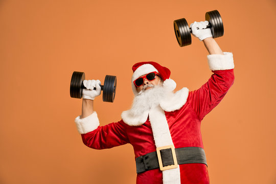 Funny bearded man in Santa costume with dumbbells above head