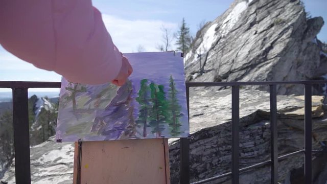 Grandmother at the peak of a winter mountain, paints a picture in oil. Woman and malbert outdoors in the new year.
