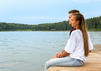 Fototapeta na wymiar A young couple a girl and a young man sit on the beach in a Lotus position on a Wooden bridge and watch the sunset. Breath of Fresh Air