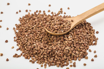 buckwheat in a plate on a white table and in a wooden spoon