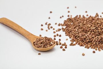 buckwheat in a plate on a white table and in a wooden spoon