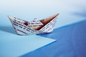 A paper boat made from old newspaper page against blue colored paper showing the concept of childhood dream, aspirations, hope and finances 