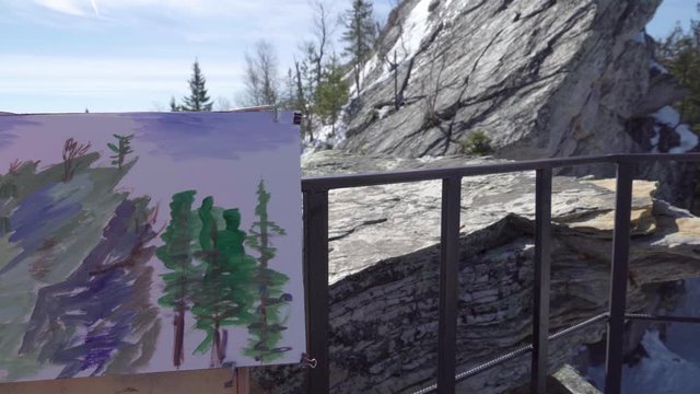 Grandmother at the peak of a winter mountain, paints a picture in oil. Woman and malbert outdoors in the new year.