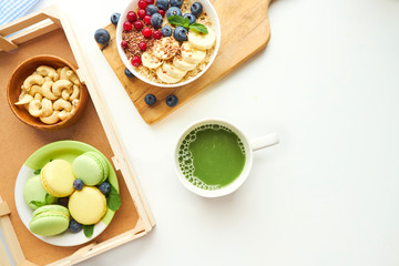 matcha green tea, breakfast top view white background. oatmeal with berries, toasts on a wooden tray, nuts, coffee