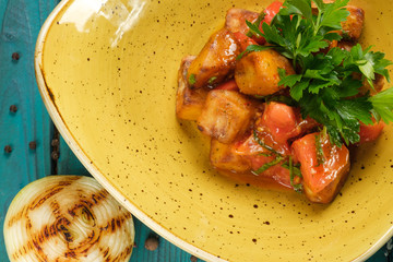 Pieces of baked pumpkin in a yellow plate decorated with parsley leaves standing on a wooden blue table