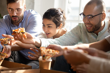 Close up happy diverse friends eating pizza together, taking slices