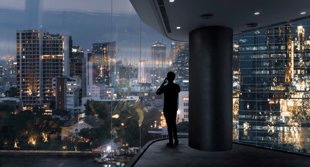 Businessman standing using smart phone in modern space watching city night view.Business with...