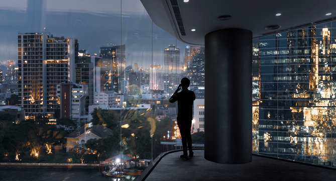 Businessman standing using smart phone in modern space watching city night view.Business with ambition and vision concept.