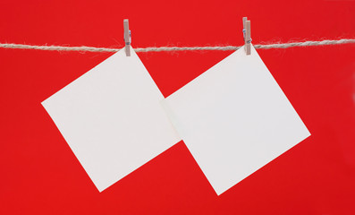Two white square piece of note paper hangs on clothespins on a red background, mock up