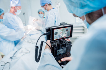 The videographer shoot the surgeon and assistants in the operating room with surgical equipment.