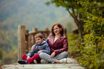 travelers family mother and son in autumn in the mountains sit on a wooden walkway