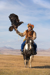 Portrait of a traditional kazakh eagle hunter with his colorful horse and majestic golden eagle on...