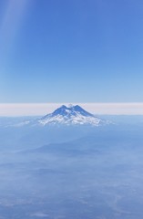 Fototapeta na wymiar Mount Rainier from airplane window with blue sky and smoky clouds