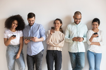 Smiling diverse people using phones, standing in row near wall