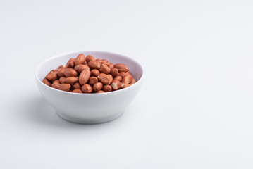 Raw shelled whole peanuts in a white bowl, isolated on white background, soft light, copy space