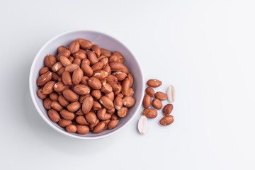 Raw shelled whole peanuts in a white bowl, isolated on white background, soft light, copy space