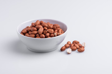 Raw shelled whole peanuts in a white bowl, isolated on white background, soft light, copy space