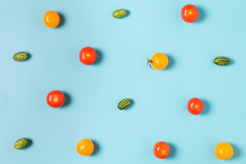 Colorful food pattern of mini cucumbers and yellow and red tomatoes on blue background. flat lay