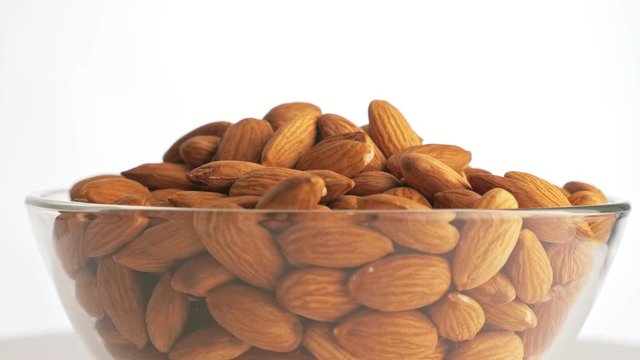 Nuts almond rotate are on a table in a plate. Snack in transparent dish on an isolated white background are spinning moving.