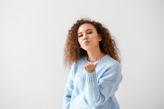 Portrait of young African-American woman blowing kiss on light background