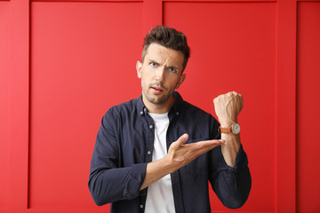 Stressed young man with watch on color background