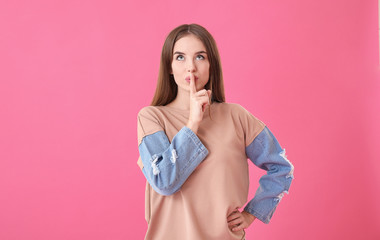 Beautiful young woman showing silence gesture on color background