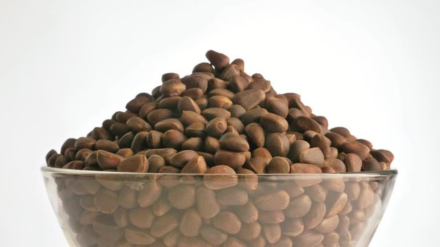 Pine nut rotate are on a table in a plate. Snack in transparent dish on an isolated white background are spinning moving.