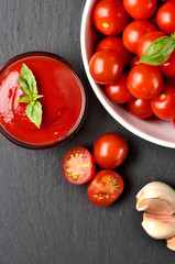 Close-up of homemade ketchup made from fresh cherry tomatoes, garlic, basil on black slate slab. Top view. Vertical photo.
