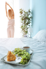 Tray with tasty breakfast on bed of young woman