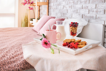 Tray with tasty breakfast on table in bedroom