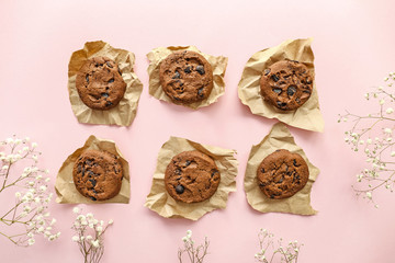 Tasty chocolate cookies and flowers on color background
