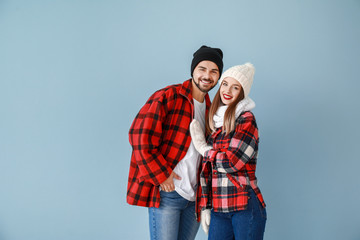 Happy young couple in warm winter clothes on color background