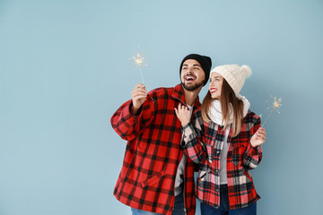 Happy young couple with Christmas sparklers on color background