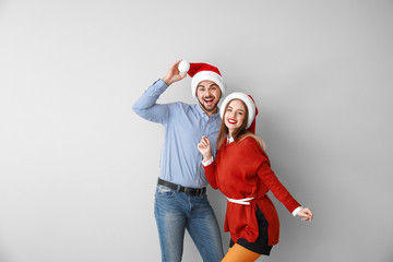Happy young couple in Santa hats on light background