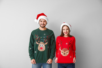 Happy young couple in Christmas clothes on light background