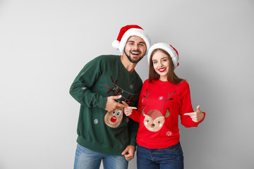 Happy young couple in Christmas clothes on light background