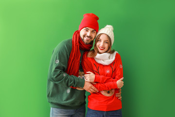 Happy young couple in Christmas clothes on color background