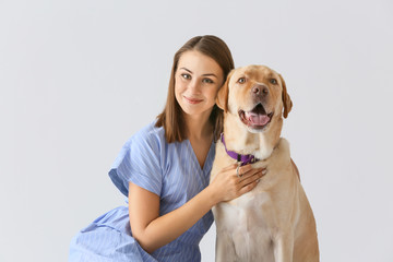 Beautiful young woman with cute dog on light background
