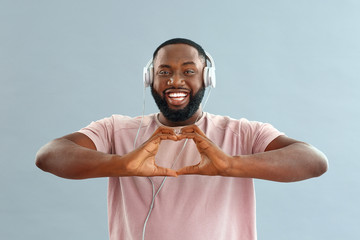 Naklejka premium African-American man making heart with his hands while listening to music on color background