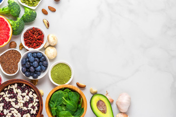 Healthy vegan food clean eating selection: fruit, vegetable, seeds, superfood, nuts, berries on white marble background