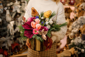 Woman holding a golden box of pink roses and crimson calla lilies decorated with pine branches and two parrots