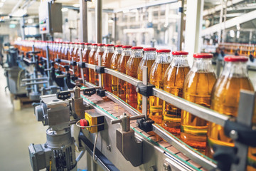 Conveyor belt, juice in glass bottles on beverage plant or factory interior, industrial...