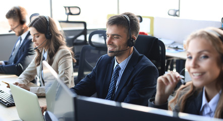 Portrait of call center worker accompanied by his team. Smiling customer support operator at work.