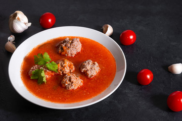 1 white plate of red tomato soup with meatballs, cilantro on a black background, garlic, fresh cherry tomatoes
