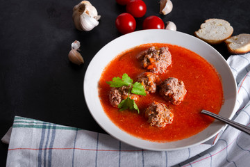 plate of red tomato soup with meatballs, garlic and cilantro on a black background, towel,