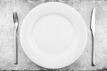 Table setting. Empty plate, knife and fork on a light concrete background. Top view and flat lay with copy space