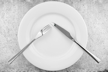Table setting. Empty plate, knife and fork on a light concrete background. Fork and knife are on the plate, pause in food. Top view and flat lay with copy space