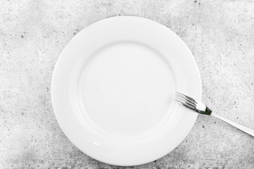 Table setting. Empty plate, fork on a light concrete background. A fork lies on a plate, a pause in food. Top view and flat lay with copy space